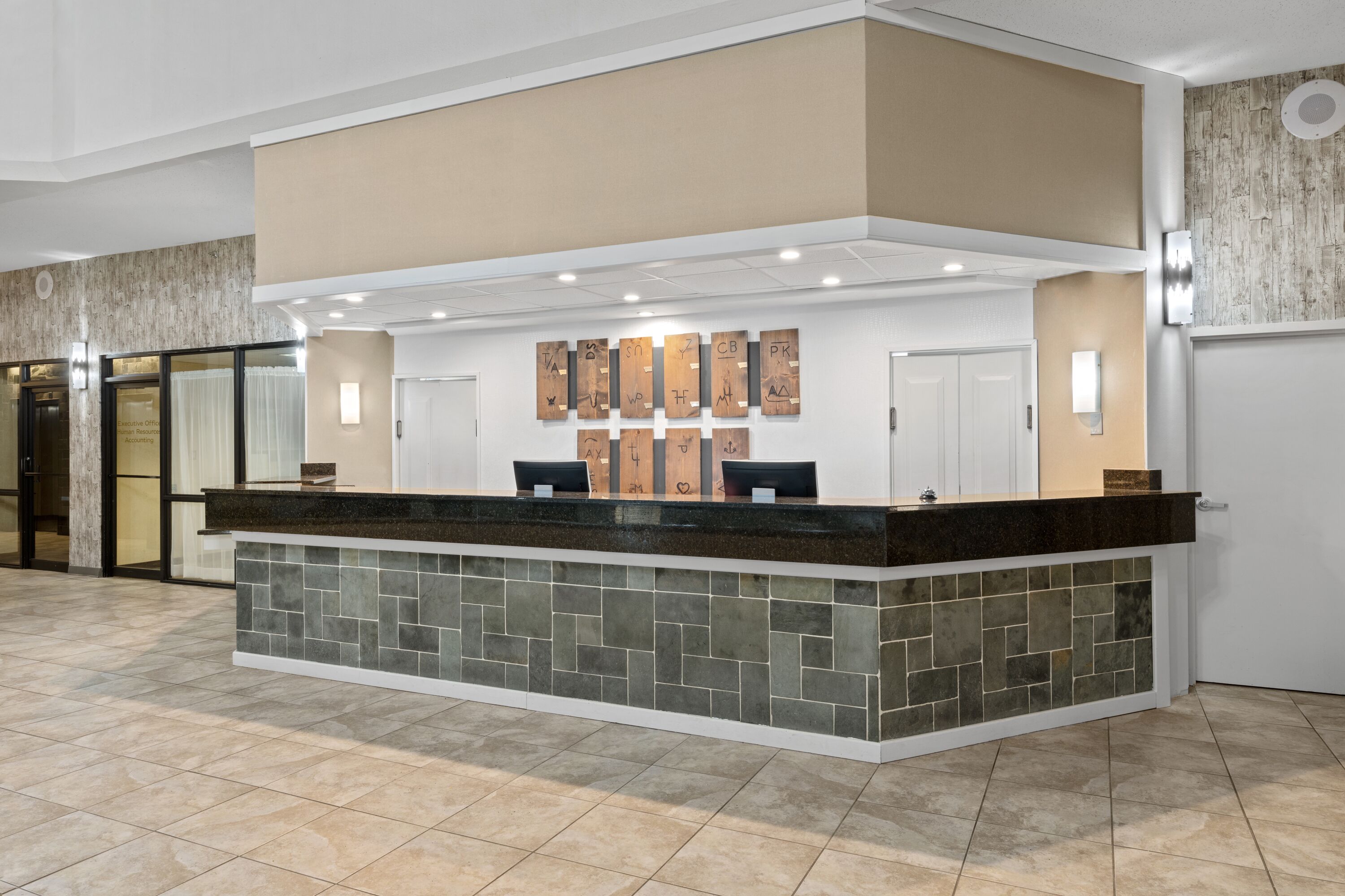 A reception desk with a stone-tiled base and a black countertop, flanked by two chairs. Above the desk, there are several wooden plaques with symbols.