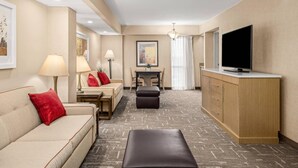 A hotel room with a sofa, ottoman, TV, and a small dining area with a table and chairs.