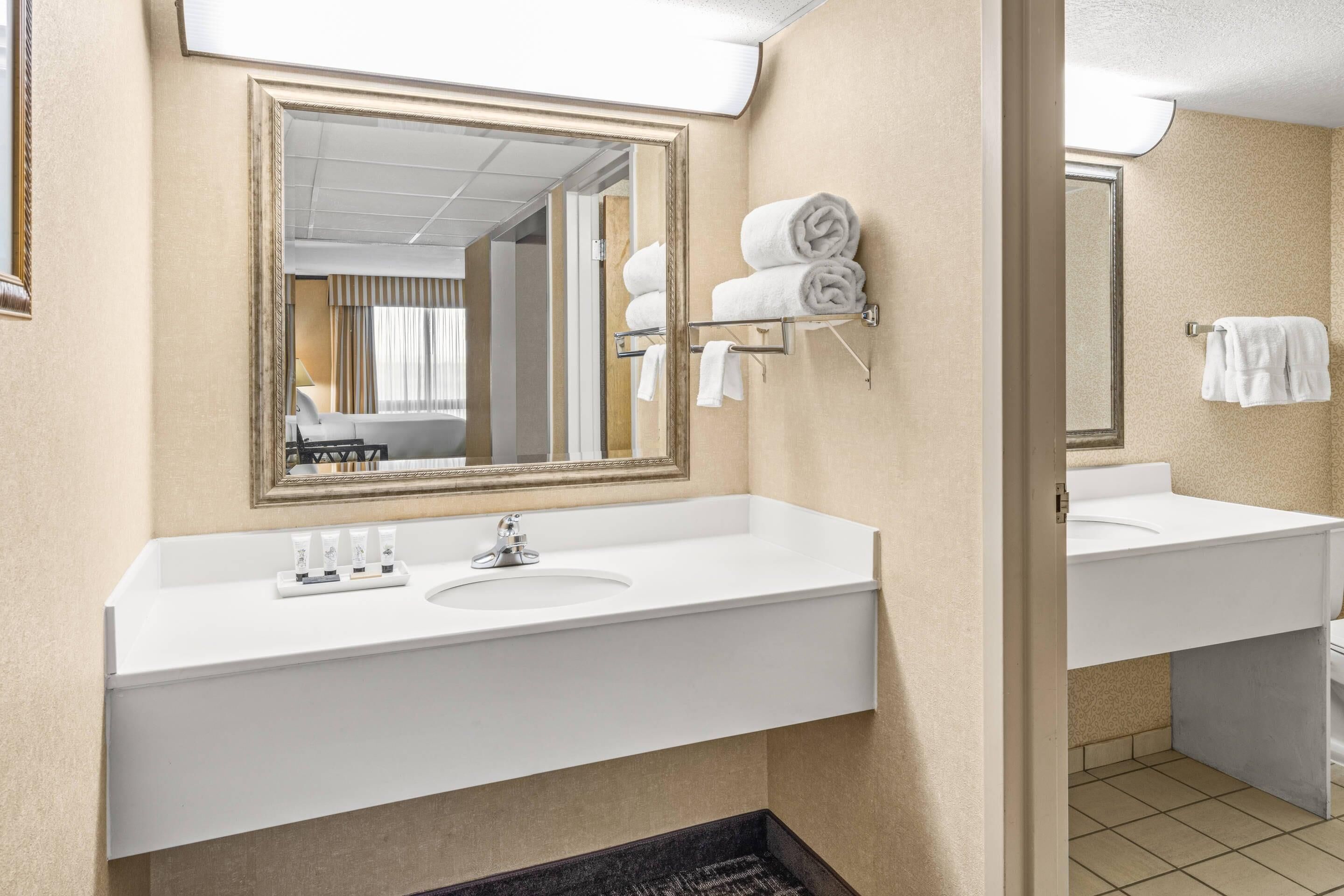 A hotel bathroom with a large mirror, two sinks, and a towel rack.