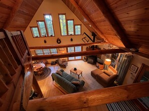 A spacious loft with a high ceiling, wooden beams, and large windows offering views of the outdoors. - Pioneer Lodge Log Cabin (Merrillan)
