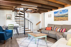 Ein Wohnzimmer mit einer Wendeltreppe aus Holz, einer Couch, einem blauen Sessel, einem Couchtisch und einem Teppich.