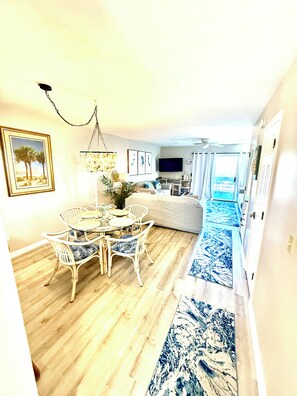 A living room with a dining area, a television, and a view of the ocean.