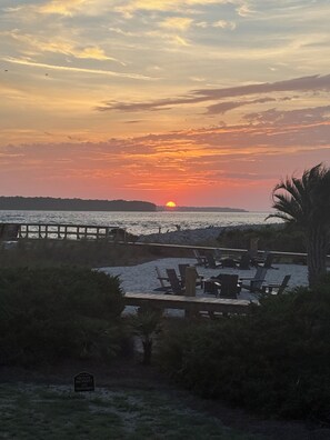 A sunset over a beach with a wooden deck and lounge chairs.
