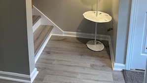A hallway with a wooden staircase, a round mirror with a textured frame, a floor lamp, and a door. - Hidden Gem on Seabrook Island-visit our fabulous beaches on this magical island! (Seabrook Island)