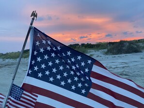 Un mât sur lequel flotte le drapeau américain, sur une plage au coucher du soleil.
