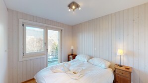 Un dormitorio con cama, mesita de noche, lámpara y ventana con vistas.