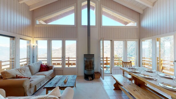 Una habitación acogedora con sofá, mesa, chimenea y ventanas amplias con vistas a la montaña.