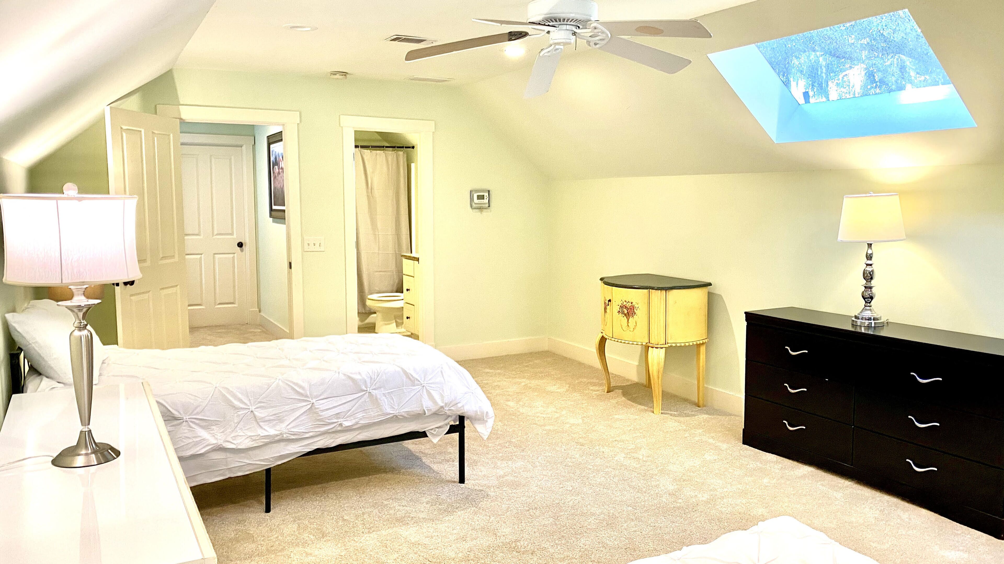 Ein Schlafzimmer mit Bett, Nachttischlampen, einem Schminktisch, einem kleinen Tisch, einem Deckenventilator und einem an der Wand montierten Fernseher.