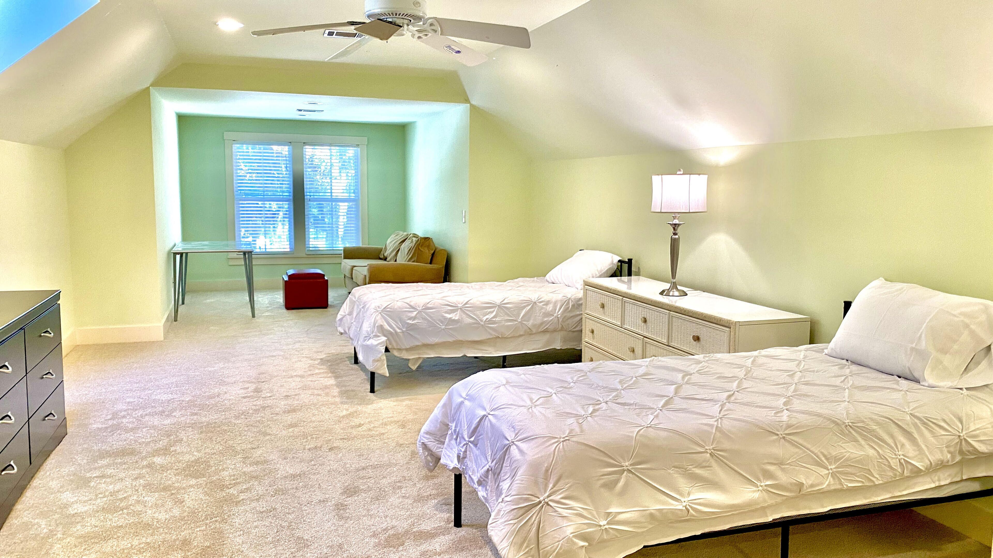 A bedroom with two beds, a desk, a chair, a dresser, and a ceiling fan.