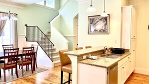 A modern kitchen with granite countertops, a built-in dishwasher, and a dining area with wooden chairs and a table. - Beautiful Cottage on Hilton Head Island, White (Hilton Head Island)