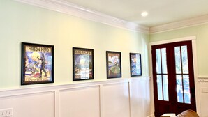 A hallway with four framed posters on the wall, a white wainscoting, and a wooden door with glass panels. - Beautiful Cottage on Hilton Head Island, White (Hilton Head Island)