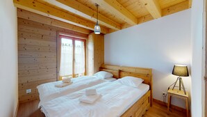 A wooden-paneled bedroom with two beds, a window with curtains, and a bedside lamp. - Des Alpes (002) - ON THE SLOPES apartment 6 pers (Haute-Nendaz)