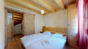 A bedroom with a wooden ceiling, a bed with white bedding, a nightstand, and a wooden door.