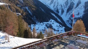 A mountain view with a ski slope, wooden tables and chairs, and a flag on a pole.