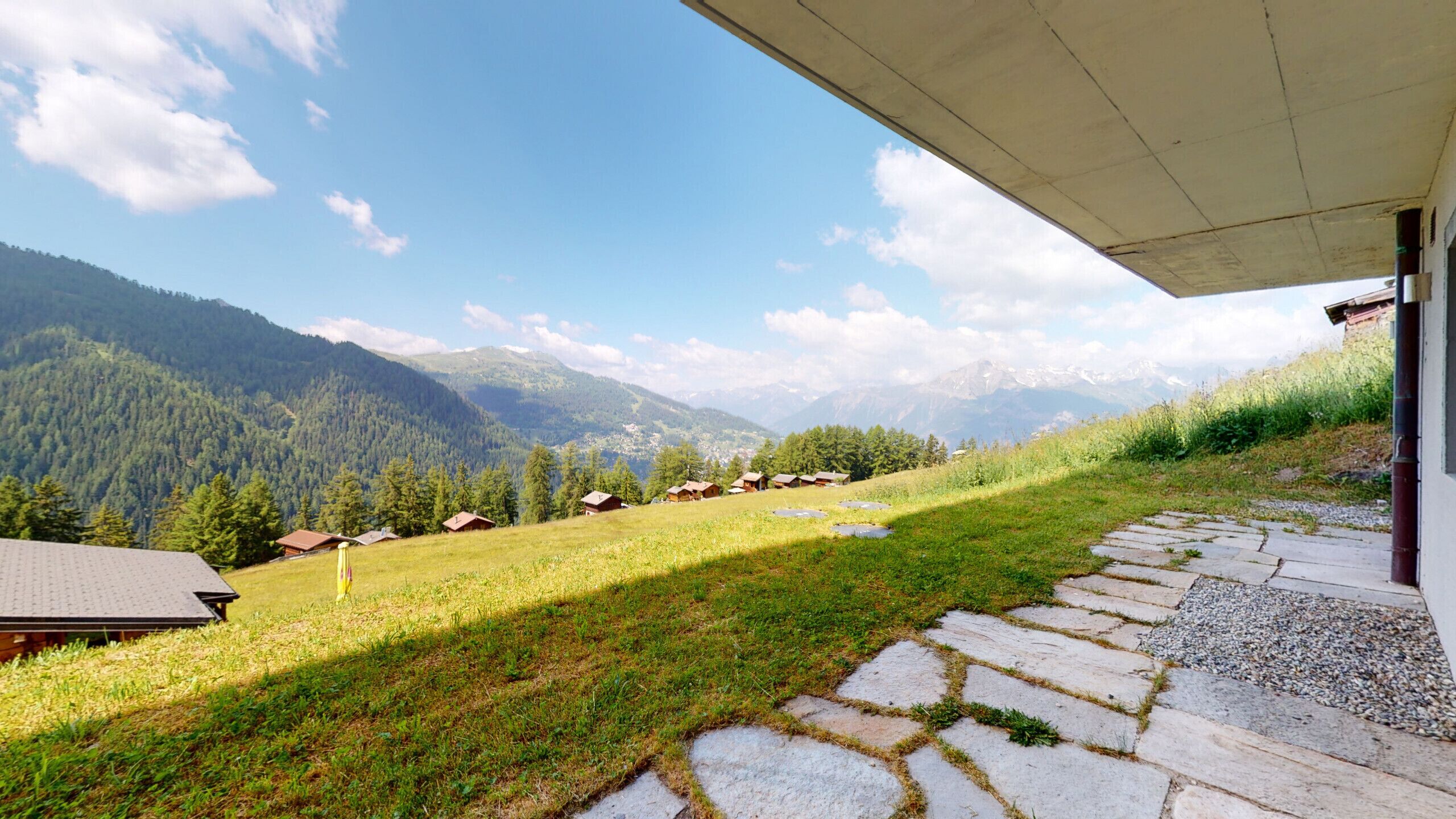 A stone pathway leading to a wooden structure with a view of a mountain range and a clear sky.