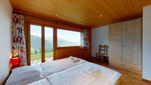 A bedroom with two beds, wooden ceiling, large windows, and a view of mountains.