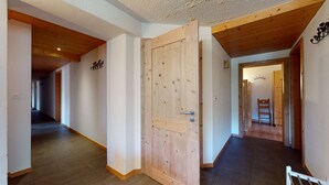 A hallway with wooden floors and walls, a wooden door, and a chair in the corner.