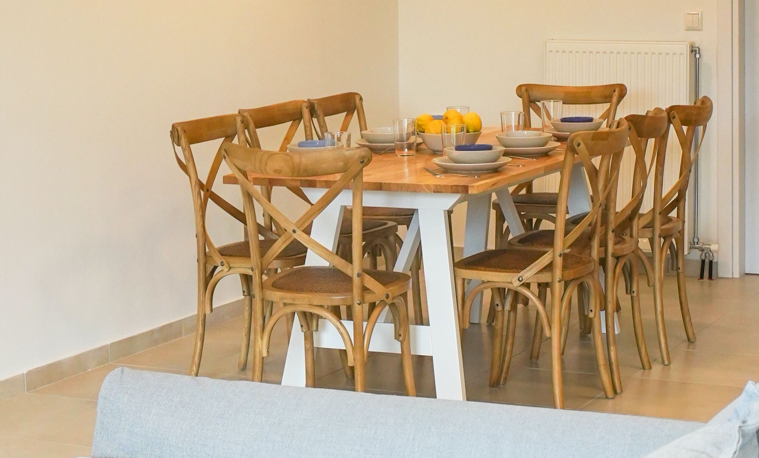 A dining area with a wooden table and chairs, a bowl of lemons, and a white radiator in the background.