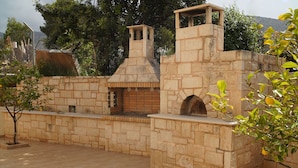 Un área de cocina al aire libre de piedra con chimenea, horno de ladrillo y un banco para sentarse.