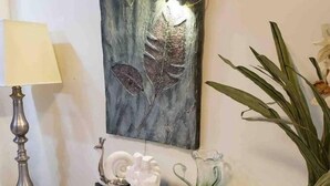 Un aparador blanco con adornos, una obra de arte en la pared y una planta en maceta.