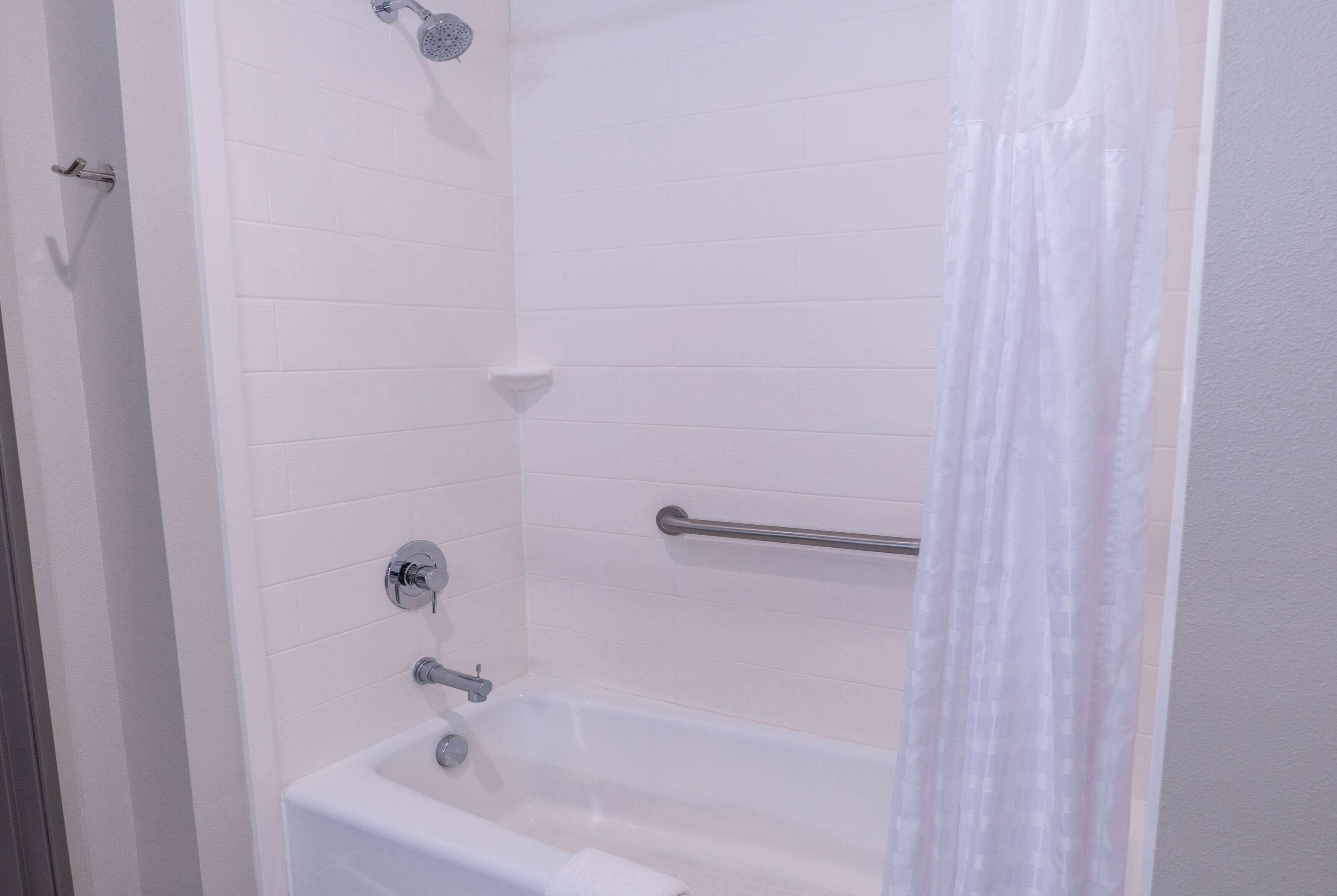 A bathroom with a white bathtub, a showerhead, a towel rack, and a glass shower curtain.
