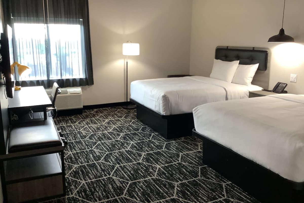 Habitación de hotel con dos camas, un escritorio, una silla, una lámpara y un calentador.