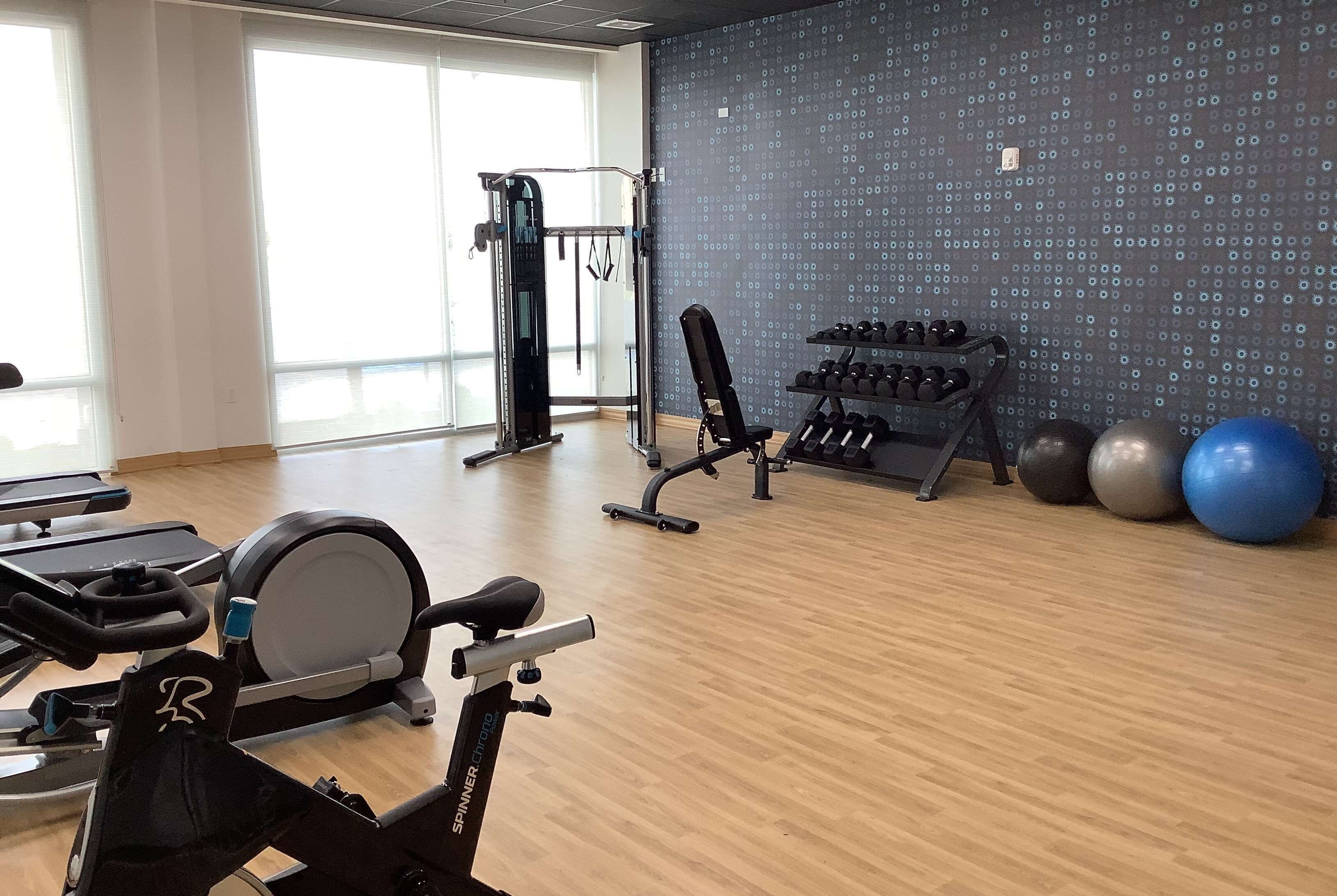 A gym with cardio equipment, dumbbells, and exercise balls.
