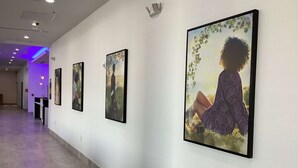 Ein Korridor mit gerahmten Kunstwerken an den Wänden und einem violett beleuchteten Bereich am Ende.