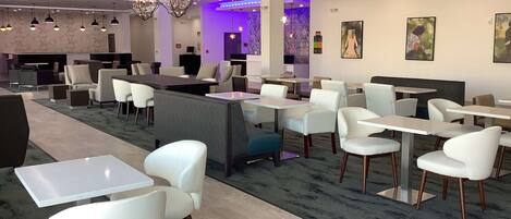 A modern restaurant with white chairs, tables, and a bar area.