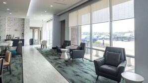 Eine geräumige Lobby mit Marmorwand, einer Sitzecke mit Stühlen und Tischen sowie großen Fenstern mit Blick auf geparkte Autos vor dem Haus.