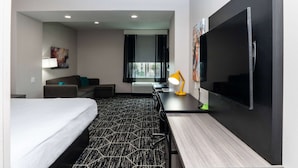 Ein modernes Hotelzimmer mit einem großen Bett, einem Schreibtisch mit Computer, einer Sitzecke, einem Fernseher und einem Fenster mit Blick.