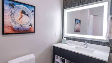 A bathroom with a white toilet, a white sink with a mirror above it, and a framed artwork on the wall.