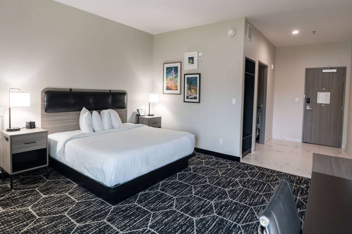 Una habitación de hotel con una cama grande, dos mesitas de noche con lámparas, una alfombra con diseño blanco y negro y una puerta a la derecha.