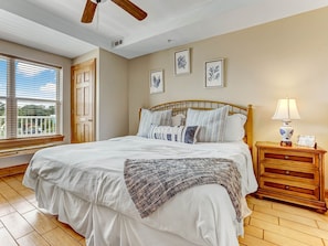 A bedroom with a bed, a wooden headboard, a nightstand with a lamp, and a window with blinds. - Community Pool | 5*Clean | Flex Cancelation (Tybee Island)