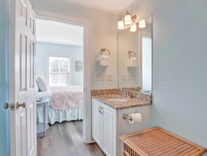 A bathroom with a vanity, a mirror, a toilet, and a wicker basket. - Heated Pool Access | Flex Cancellation (Tybee Island)