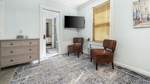 A bedroom with a large window, a flat-screen TV, a dresser, and a chair. - Nibley Park Sugarhouse Bungalow (Salt Lake City)