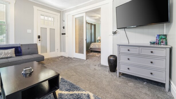 A modern living room with a grey sofa, a coffee table, a TV mounted on the wall, and a grey carpet. - Nibley Park Sugarhouse Bungalow (Salt Lake City)