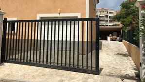 A building with a beige facade, a black metal gate, and a tiled patio area. - Location Villa (Fréjus)
