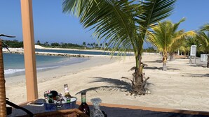 A beachside patio with a wicker basket containing bottles and glasses, a KFC cup, and a table set for two. - Luxury Private Beachfront Escape (Ocho Rios)