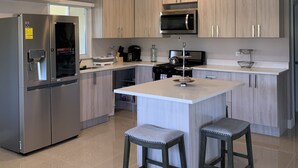 A modern kitchen with light wood cabinets, stainless steel appliances, and a central island with stools. - Luxury Private Beachfront Escape (Ocho Rios)