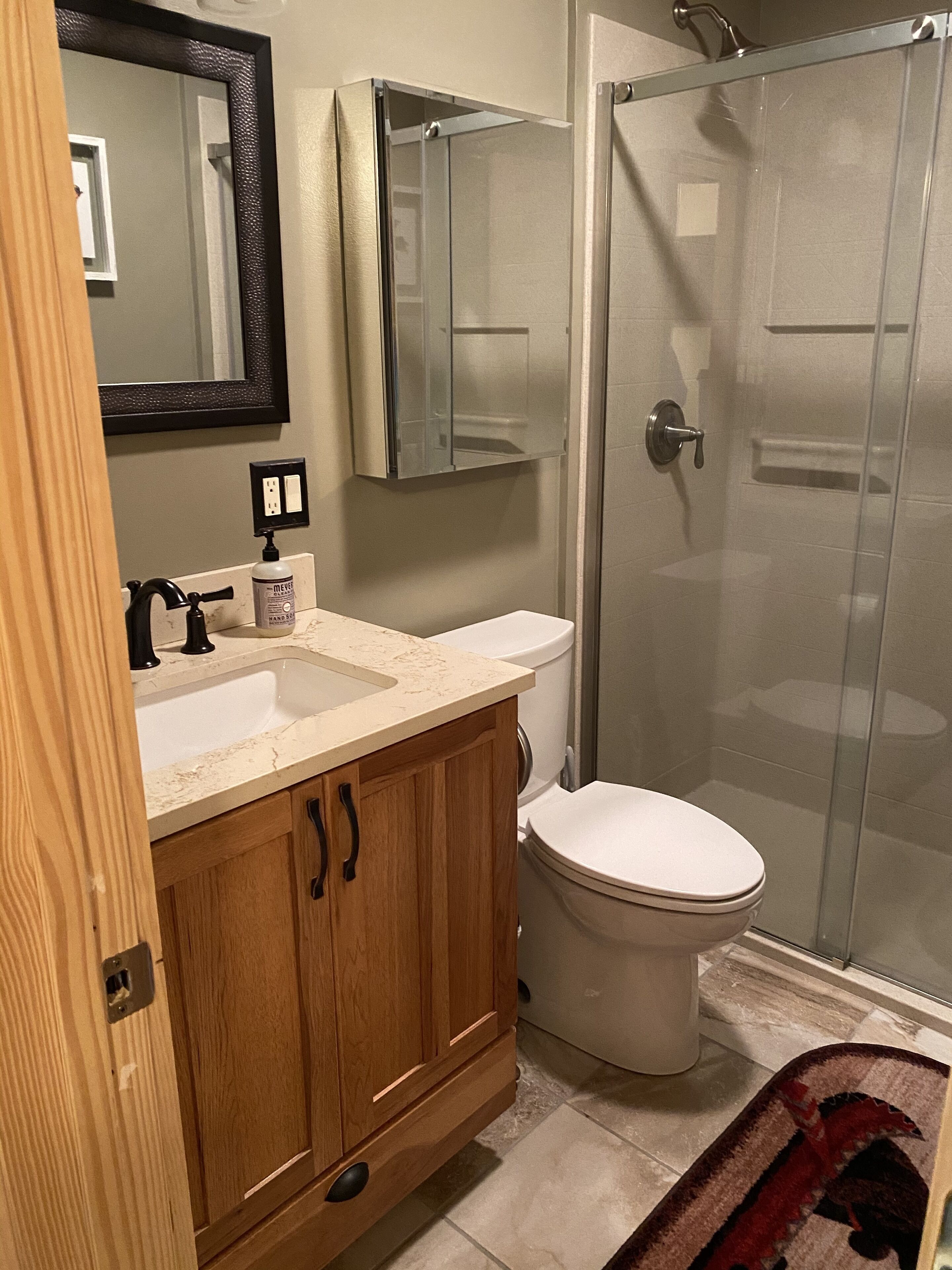 A bathroom with a wooden vanity, a white toilet, a glass shower enclosure, and a mirror above the sink.