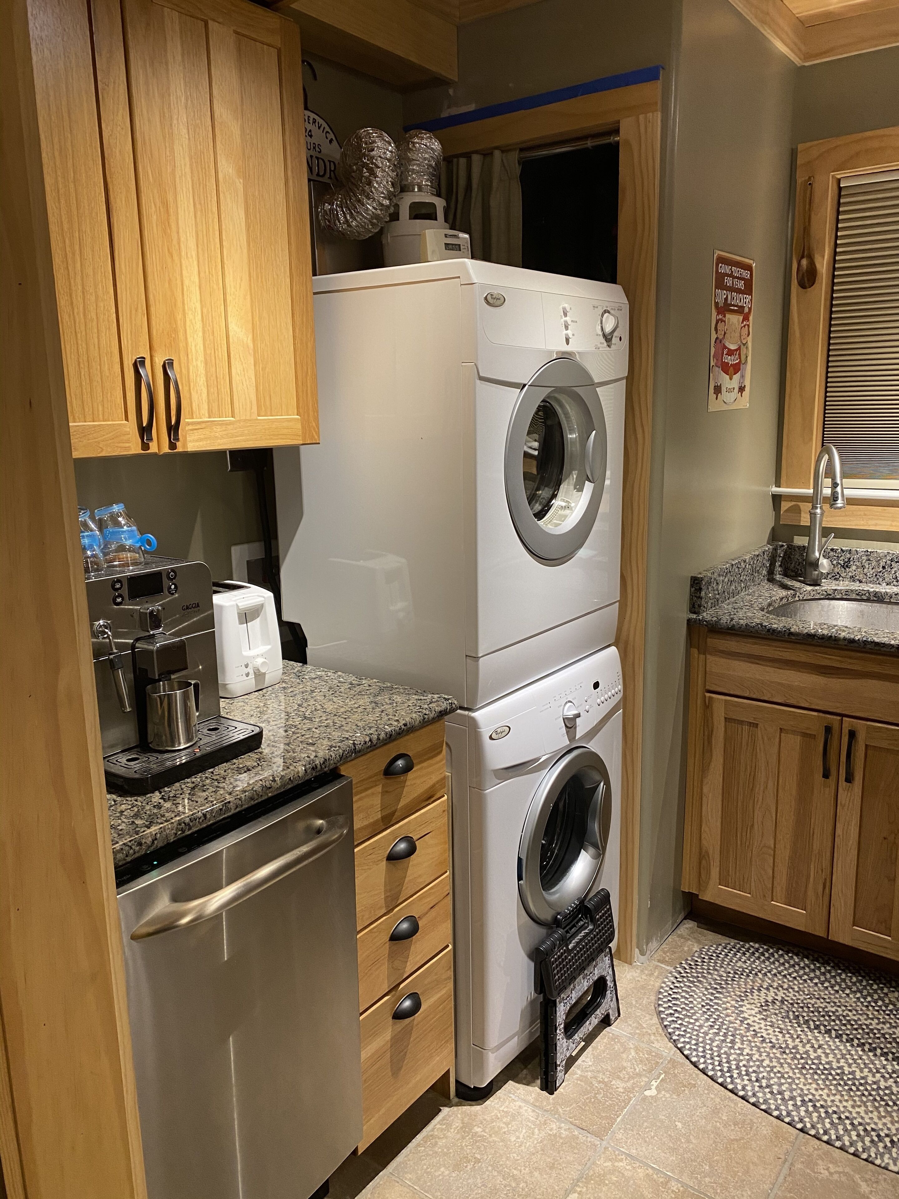 Een kleine wasruimte met een wasmachine en droger boven elkaar, een koffiezetapparaat en een klein wastafeltje.
