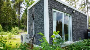A modern building with a stone exterior, large glass windows, and an air conditioning unit attached to the side. - Tiny House on the River with Wifi, Sauna and Hot Tub. (Burks Falls)
