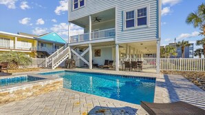 A two-story building with a swimming pool, outdoor seating, and a covered patio area. - Shore Beats Work 6BR 5BA Beach Home with Outdoor Pool, Hot tub, and Game Room (North Myrtle Beach)