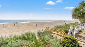 A beach with a wooden staircase leading down to the shore, a sandy beach, and the ocean in the background.