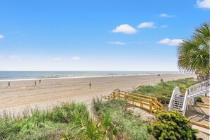 Une plage avec un escalier en bois descendant jusqu’au rivage, une plage de sable et l’océan en arrière-plan.