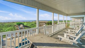 A covered deck with white railings, a pool, and beach views.