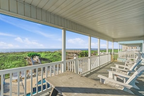 A covered deck with white railings, a pool, and beach views.