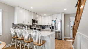 A modern kitchen with white cabinets, a central island, bar stools, and stainless steel appliances.