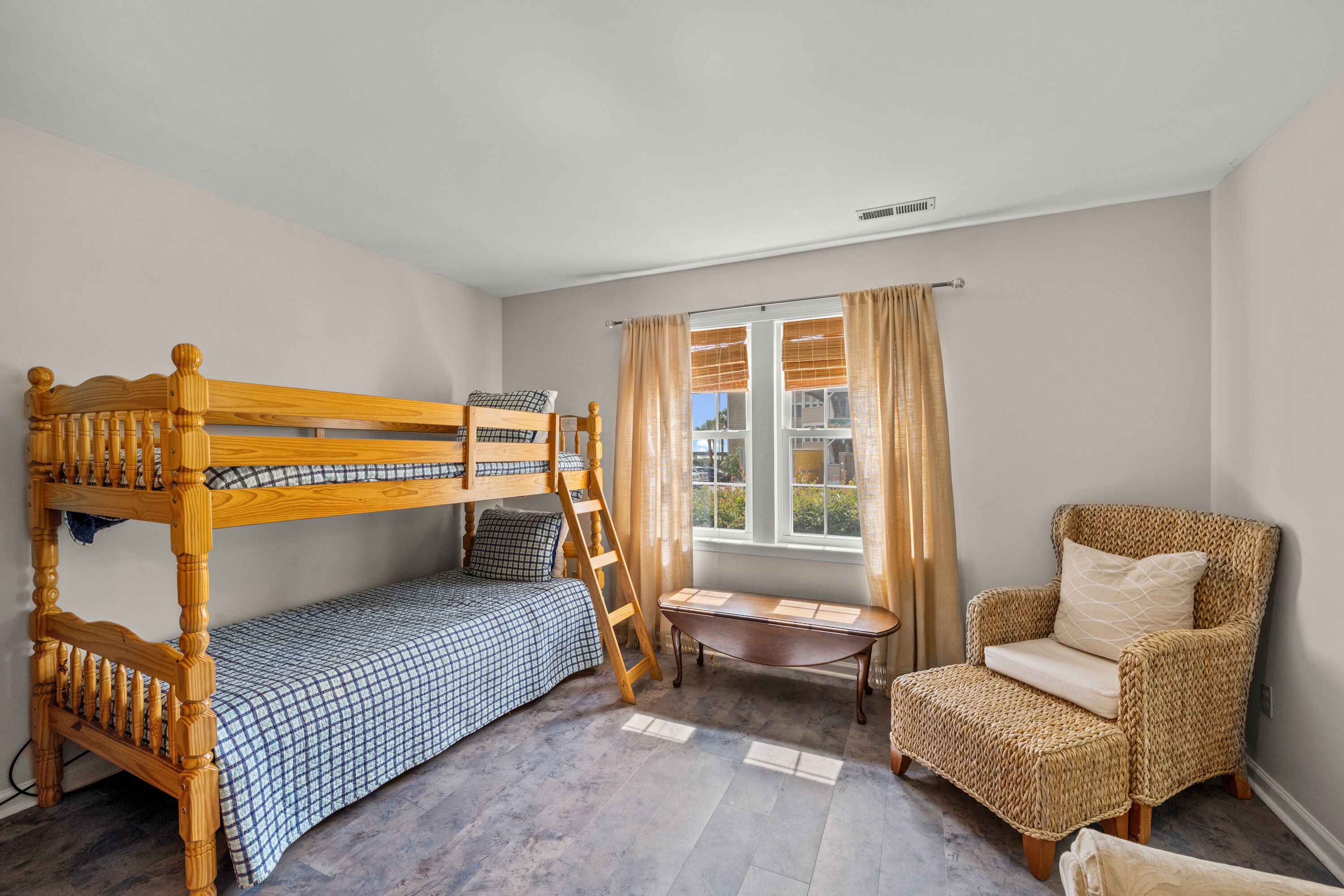 A bedroom with a bunk bed, a chair, a small table, and a window with curtains.